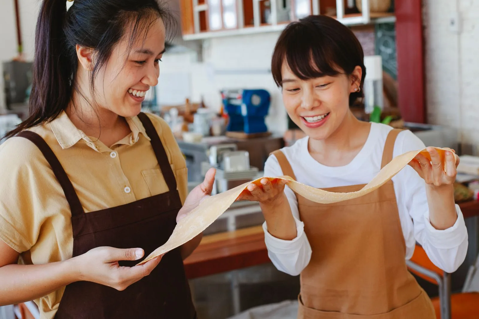 Two adults smiling as they stretch dough together in a hands-on baking class