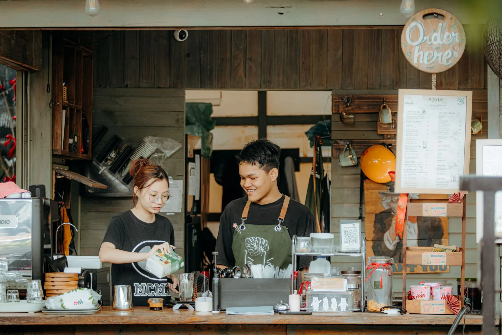 Two smiling café staff preparing an order together at a busy counter