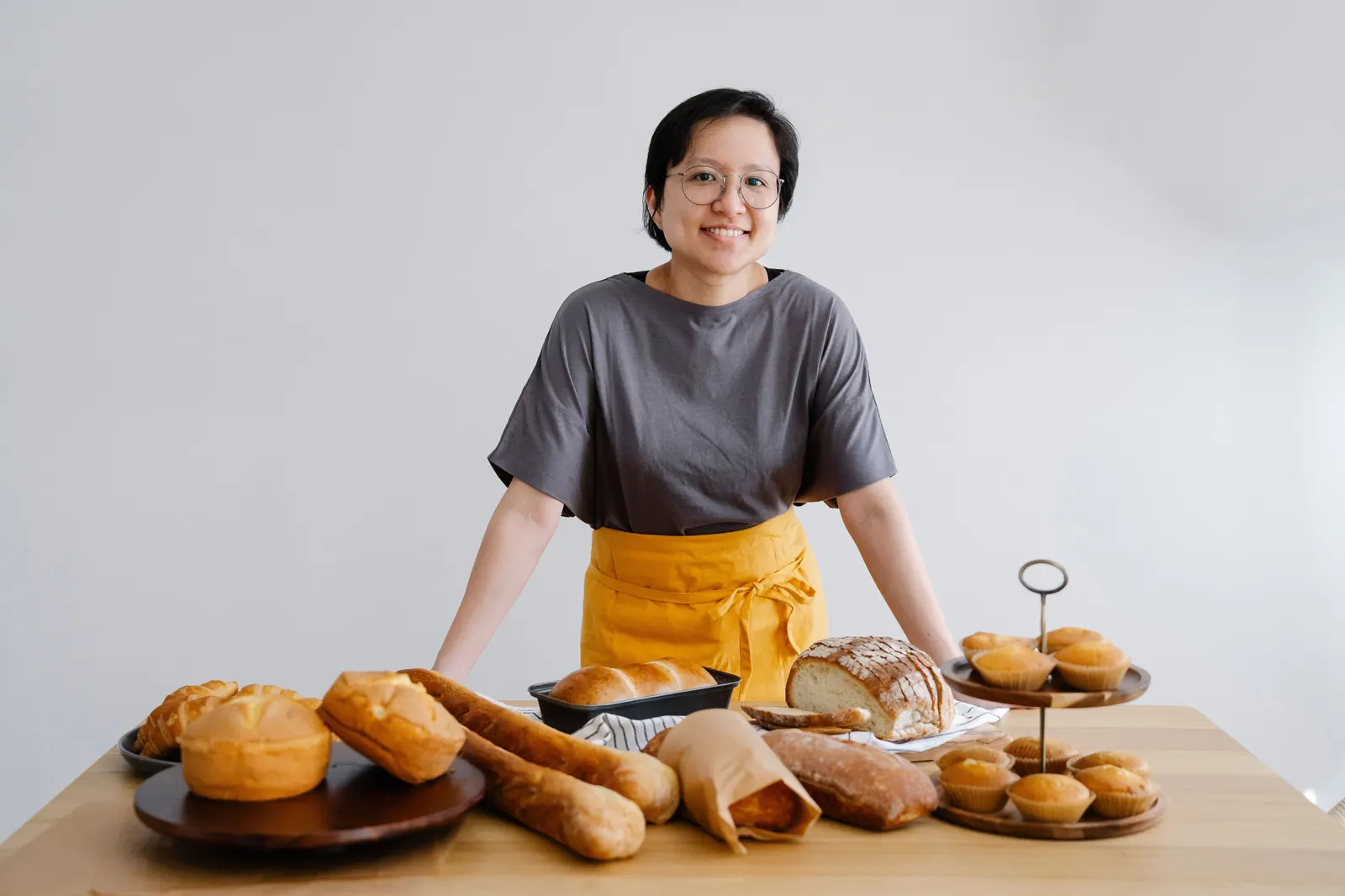 Smiling baker standing behind a table of freshly baked bread, baguettes, and muffins