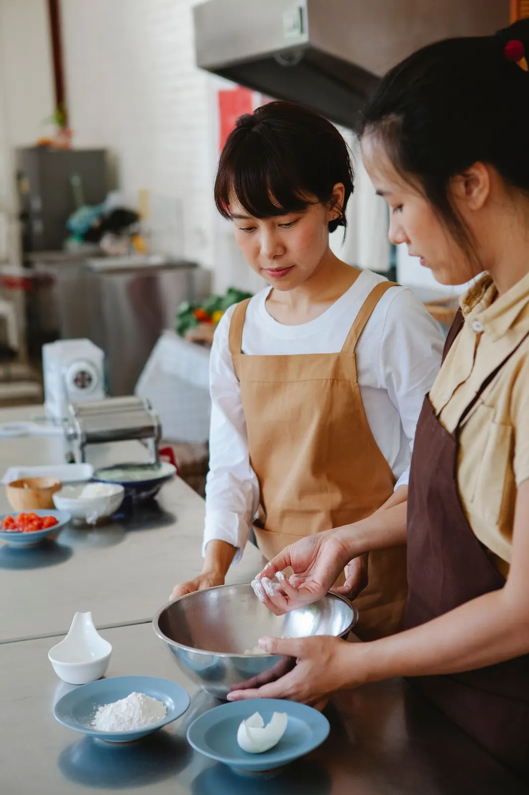 An instructor guiding a student's hands while kneading dough together at a kitchen counter